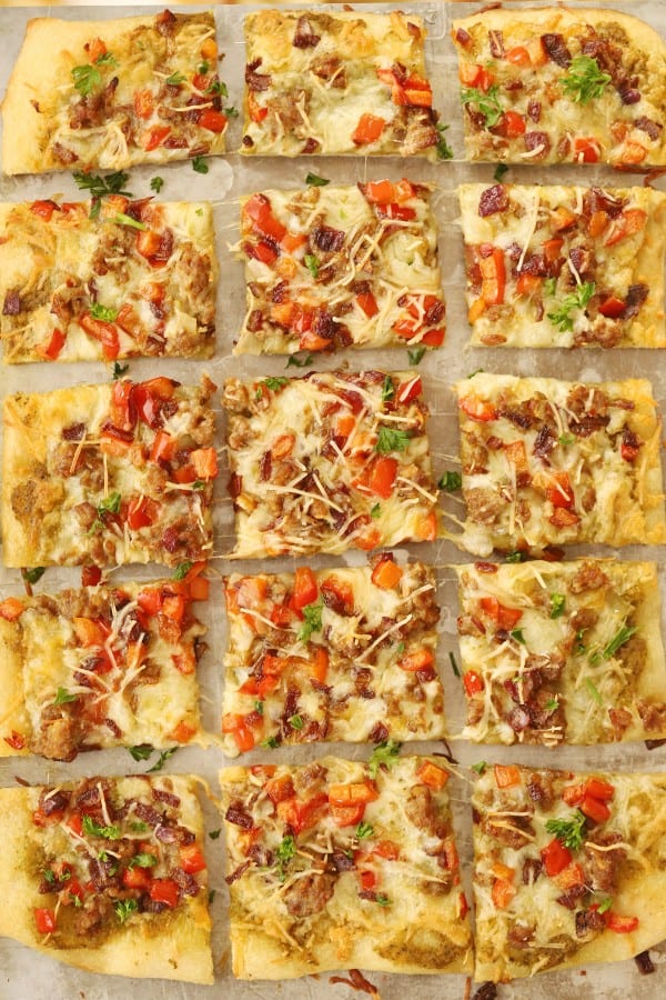homemade sausage flatbread cut into squares on a baking sheet.