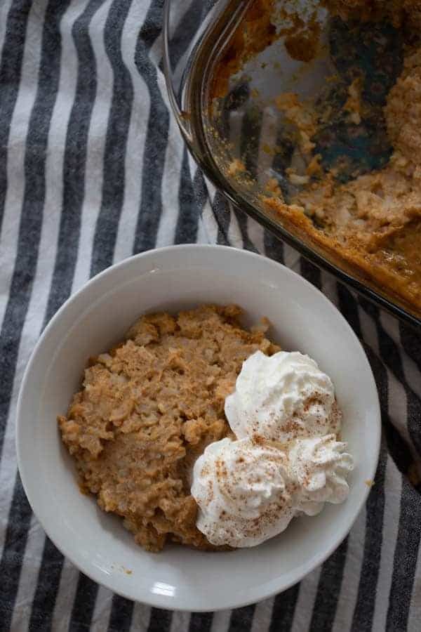 A white bowl filled with pumpkin rice pudding that is topped with whipped cream and cinnamon. Pumpkin rice pudding with leftover rice, leftover rice dessert, pumpkin rice dessert recipe.