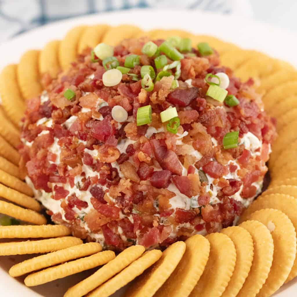 Bacon ranch cheese ball topped with sliced green onions and surrounded by crackers.