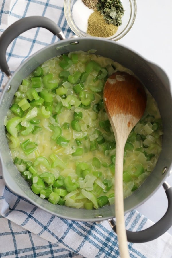 Celery, onions and butter in a pot with a wooden spoon.