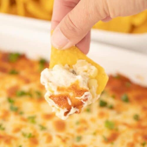Easy Fiesta Corn Dip in a baking dish with a hand dipping a chip into it.