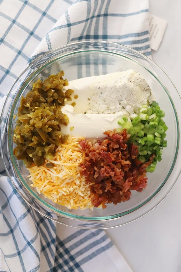 Jalapeno cheese ball ingredients in a glass mixing bowl on a tabletop.