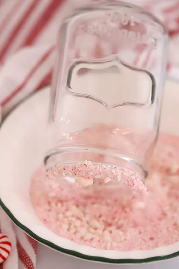 A mason jar rim dipped into a bowl full of candy cane pieces.