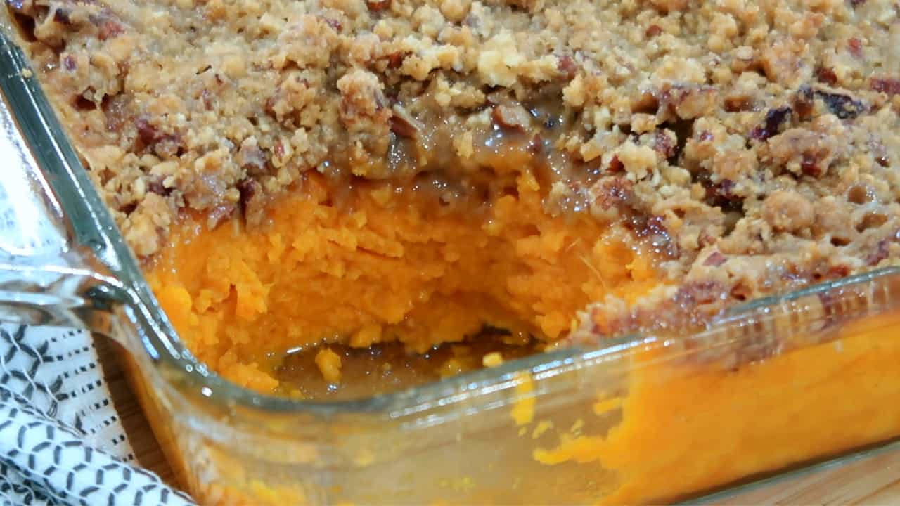 Sweet potato casserole with pecan topping in a baking dish with a serving removed. Sweet potato crumble. Sweet potato casserole with crumble topping.