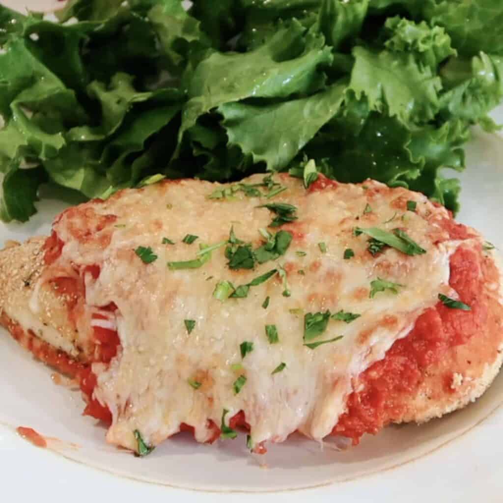 oven baked chicken parmesan recipe on a plate with salad