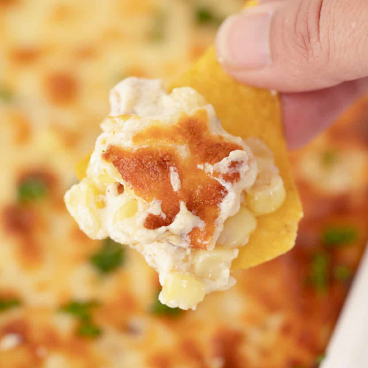 Easy Fiesta Corn Dip in a baking dish with a hand dipping a chip into it.