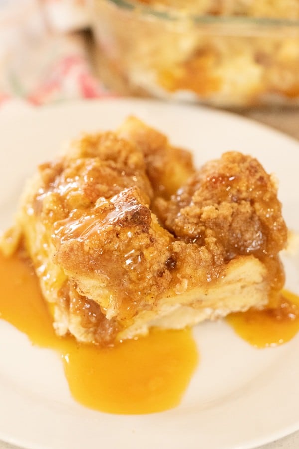 Apple French Toast Casserole on a white serving plate, covered with syrup.