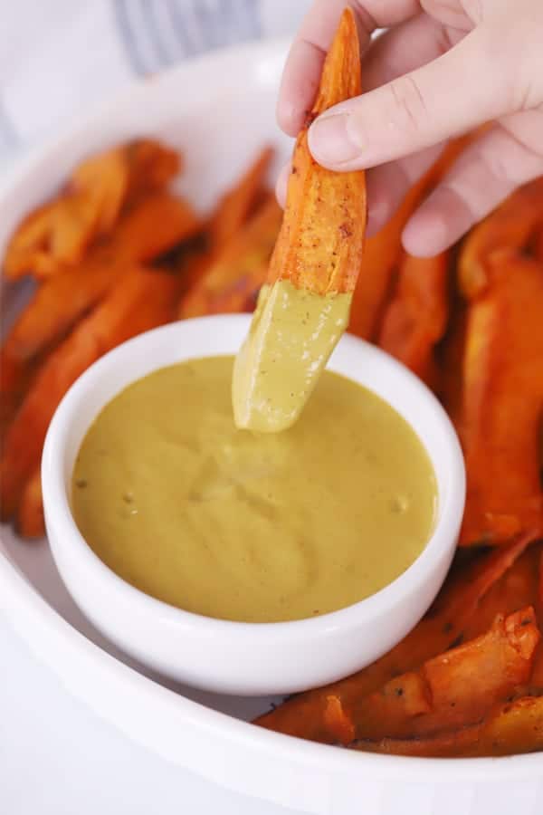 the best dip for sweet potato fries in a small ramekin with a hand dipping sweet potato fries into the sauce.