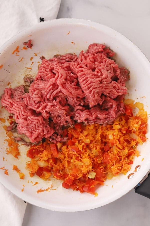 raw ground beef, carrots, bell peppers and onions in a saute pan