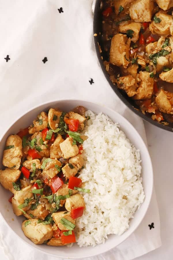 A serving bowl filled with white rice and thai chicken and basil stir fry.