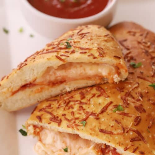 Homemade calzones on a serving dish with a side of marinara sauce.
