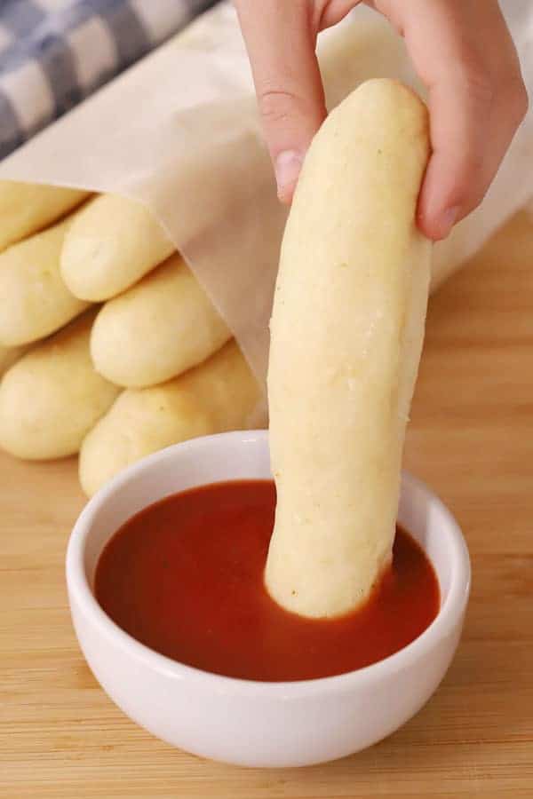 a hand dipping a copy cat olive garden breadstick into a bowl of marinara sauce