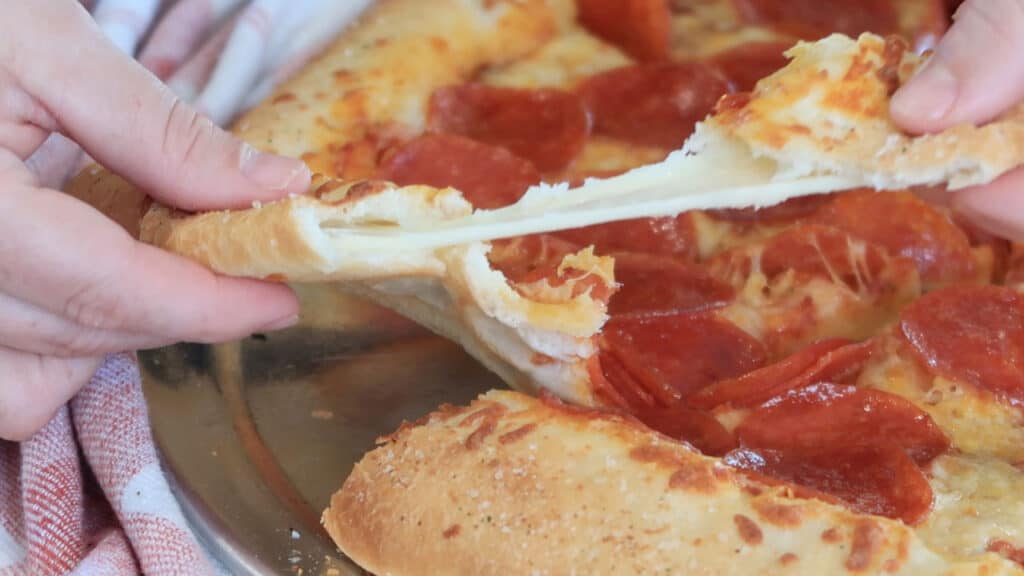 Hands pulling apart the crust of a stuffed pizza showing the cheese inside.