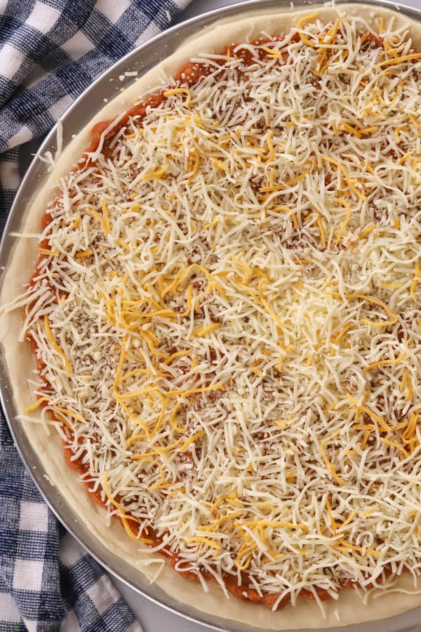pizza Dough spread onto a pizza pan topped with pizza sauce and cheese.