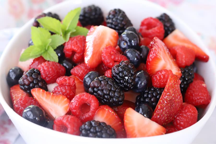 Berry salad in a white bowl garnished with mint leaves.
