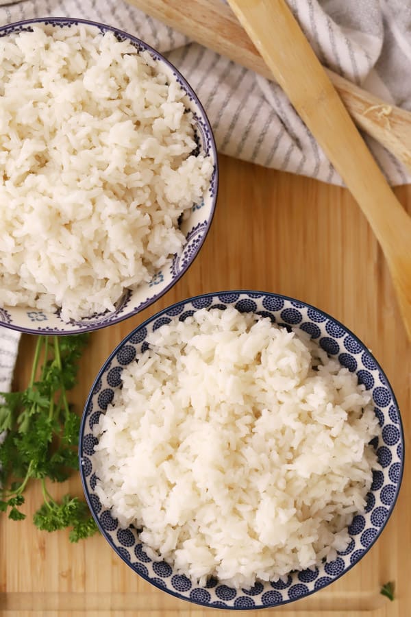 Two bowls of coconut rice on a table with fresh cilantro on the side.