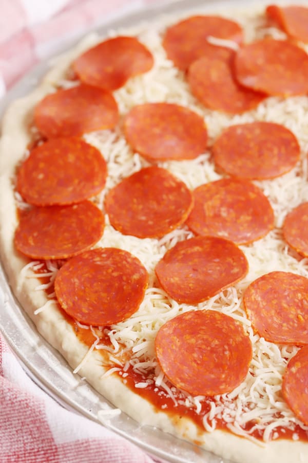 Pizza dough spread onto a pizza pan topped with sauce, cheese and pepperoni. how long to cook homemade pizza, temperature for pizza dough.