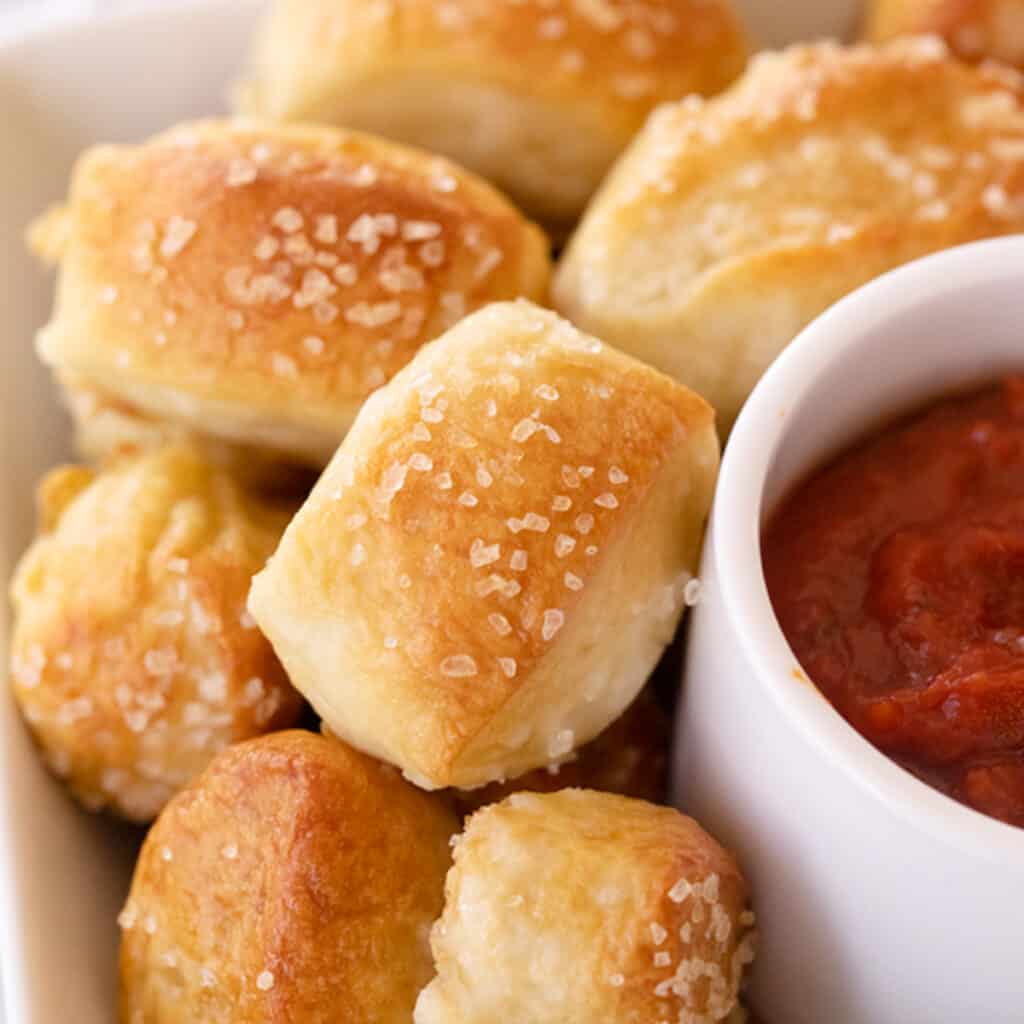 Pretzel bites on a serving dish with a side cup of marinara sauce. Great easy appetizers.
