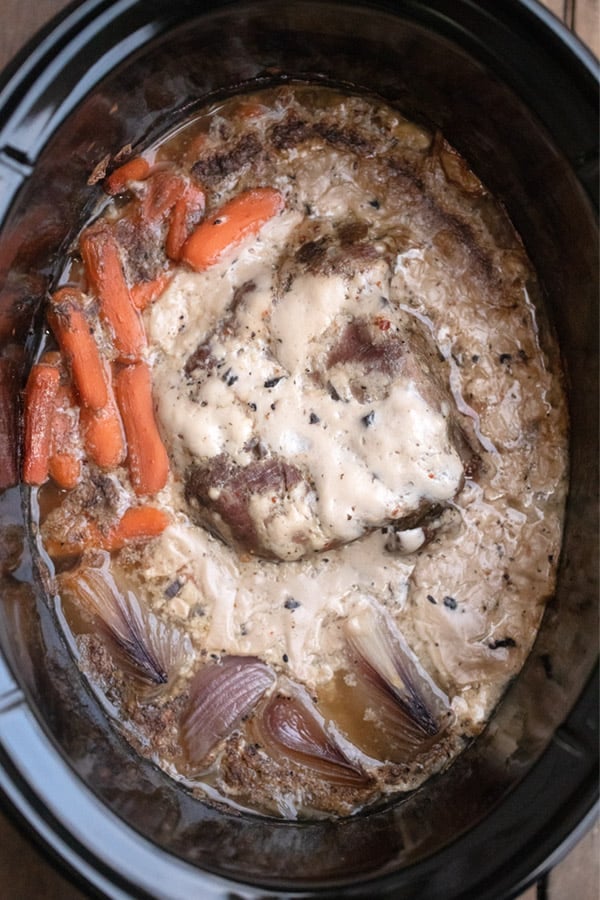 crock pot venison roast cooking in a slow cooker along with carrots and onions, venison roast crock pot, venison roast slow cooker, deer roast in crock pot.