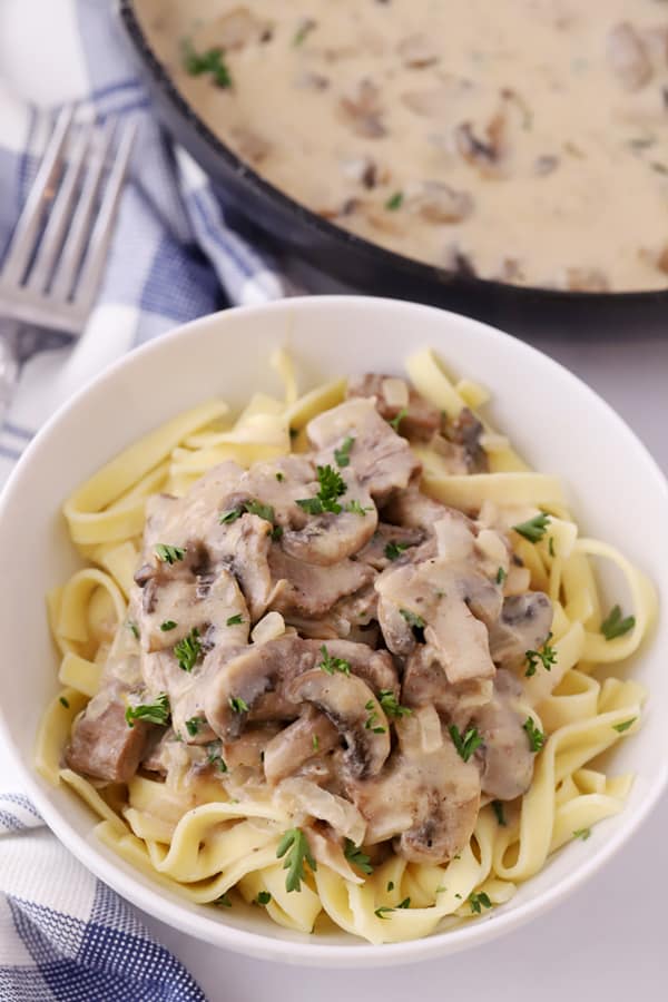 beef stroganoff in a white bowl served over egg noodles.