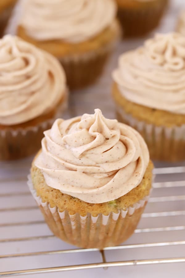 Healthy zucchini cupcakes topped with cinnamon buttercream frosting on a wire cooling rack.