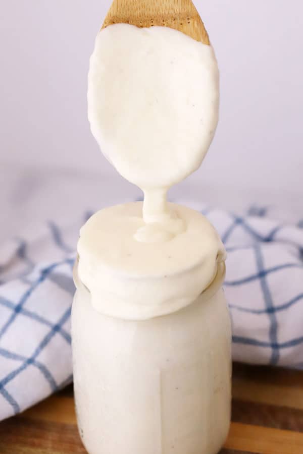 A wooden spoon with Alfredo sauce dripping into a jar.