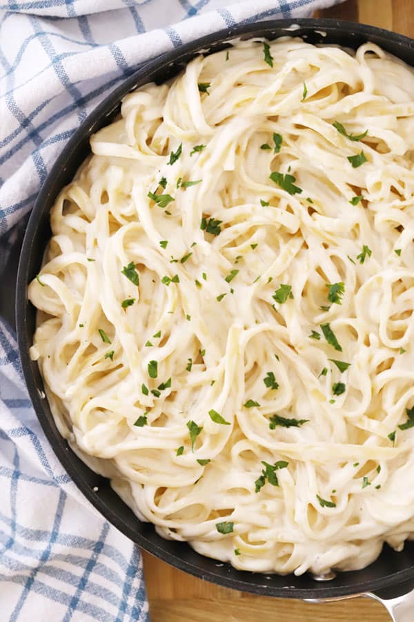Fettuccini Alfredo in a saute pan, garnished with fresh parsley.