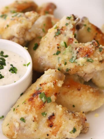 Garlic Parmesan chicken wings on a serving platter with a side bowl of dipping sauce.