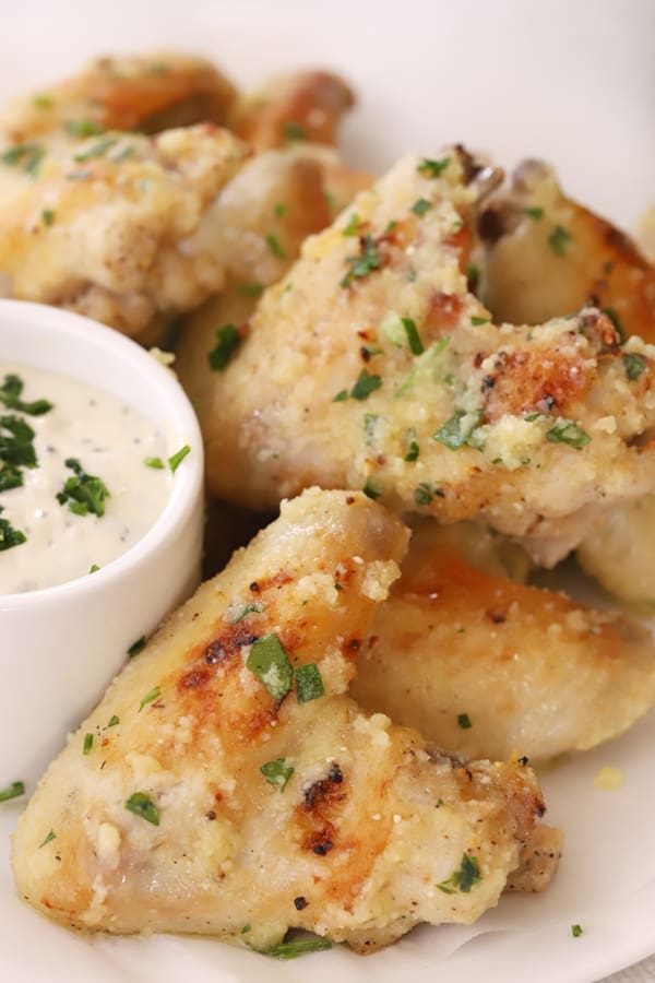 Garlic Parmesan chicken wings on a serving platter with a side bowl of dipping sauce.