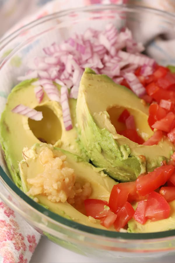 Avocadoes, red onion and tomatoes in a bowl ready to make guacamole.