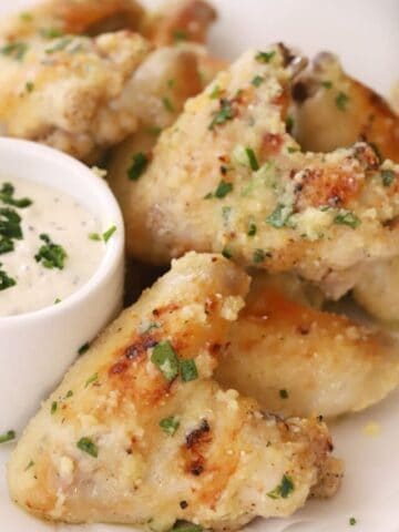 baked Garlic Parmesan chicken wings on a serving platter with a side bowl of dipping sauce, garlic parmesan wings recipe.