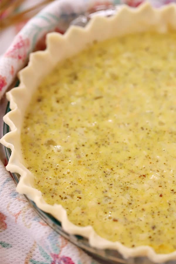 unbaked pesto quiche in a pie crust, ready to be baked, cheese in pesto.