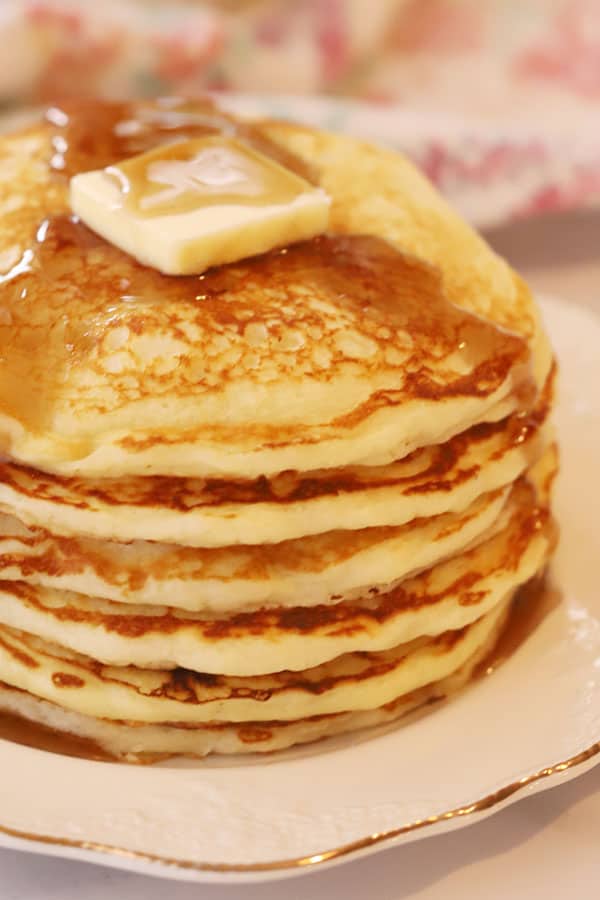 stacked fluffy buttermilk pancakes on a white plate. 