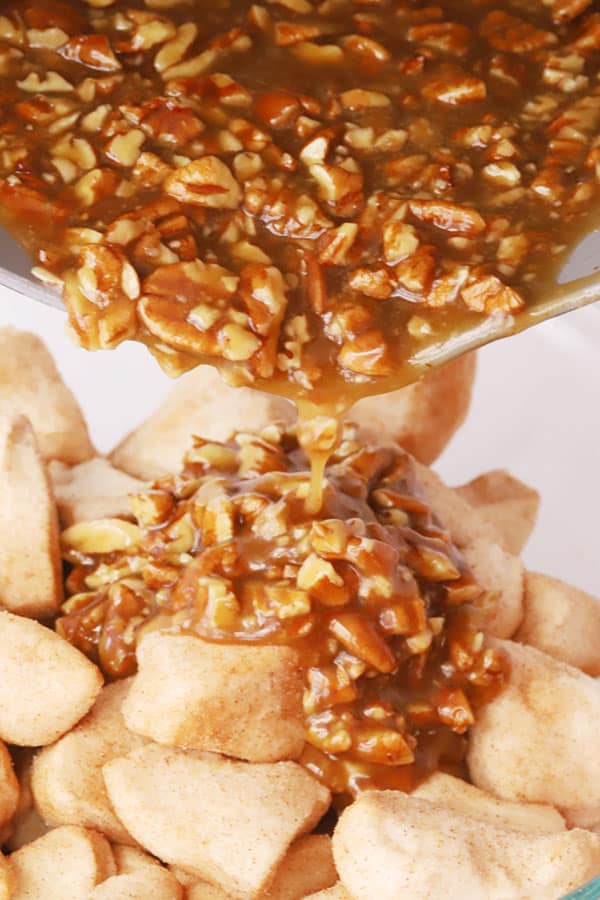 Caramel with pecans being poured over biscuit pieces to make monkey bread.