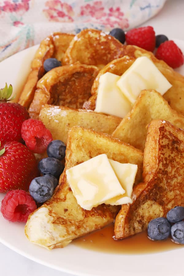 Classic french toast recipe, stacked on a plate with berries, butter and syrup