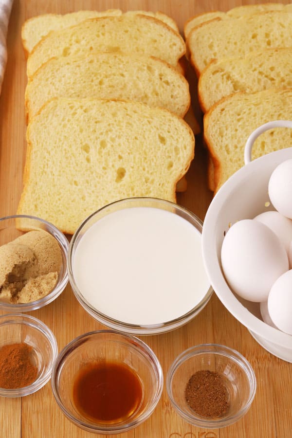 Ingredients for French Toast on a table (including sliced bread, milk, brown sugar, spices, eggs and vanilla).