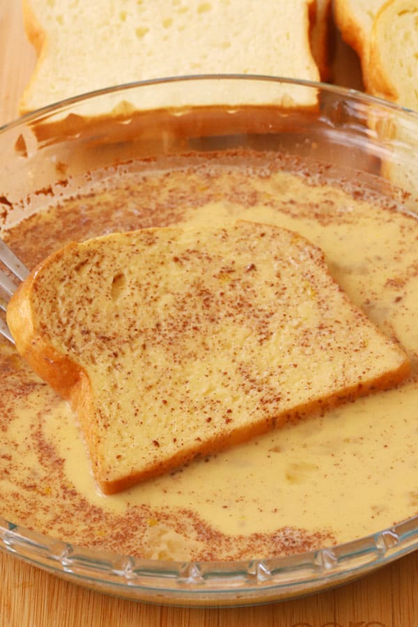 A slice of bread being dipped into cinnamon egg mixture for French Toast.