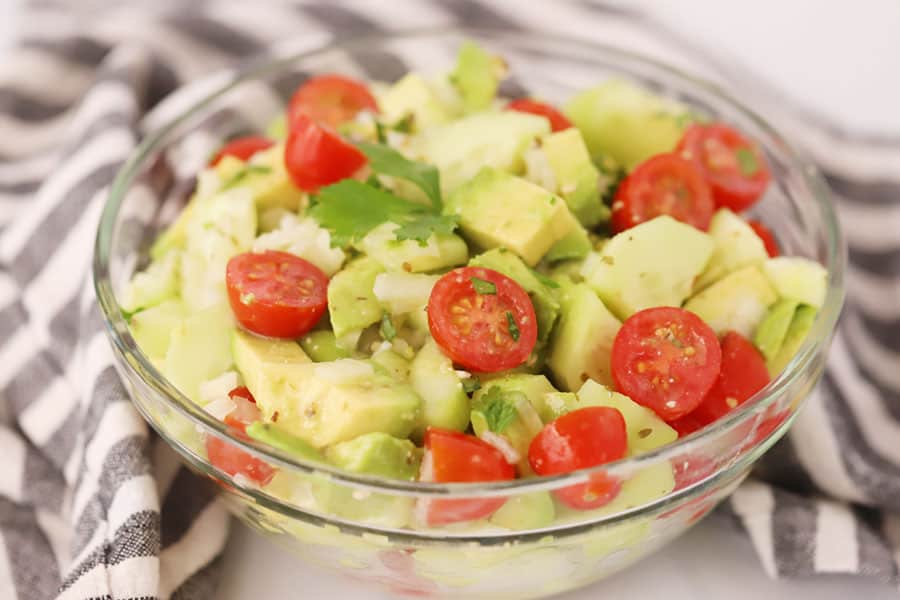 Avocado cucumber salad in a large serving bowl topped with tomatoes.