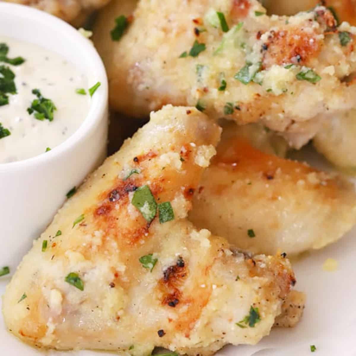 baked Garlic Parmesan chicken wings on a serving platter with a side bowl of dipping sauce, garlic parmesan wings recipe.