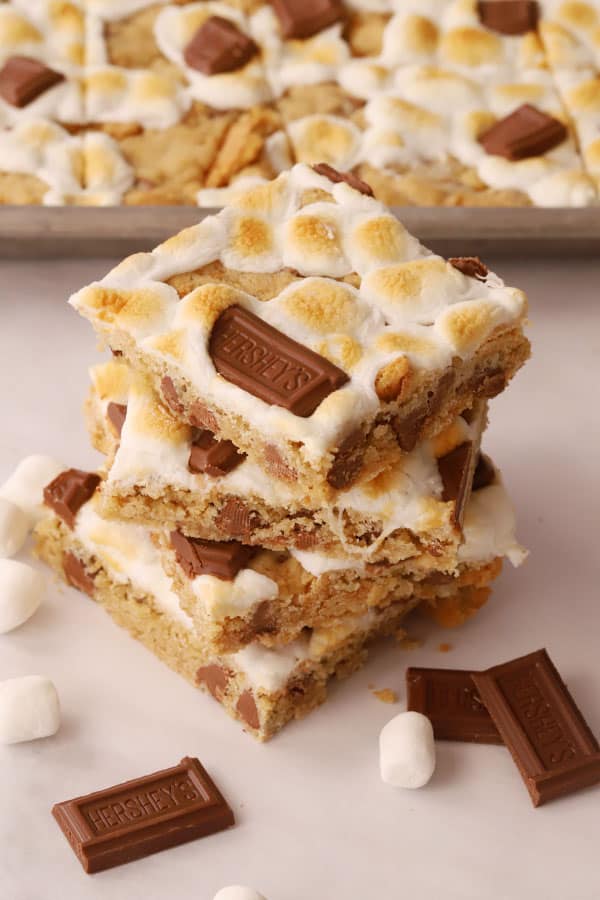 S'mores cookie bars stacked, decorated with marshmallows and Hershey's chocolate squares.