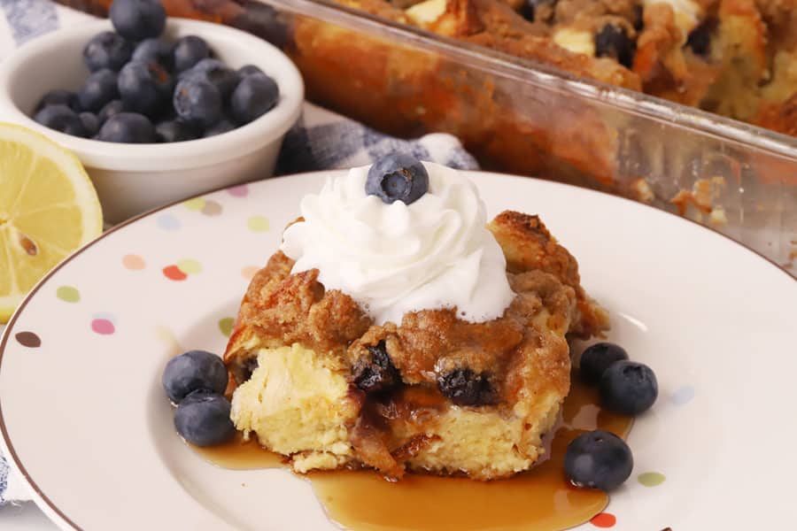 baked blueberry french toast bake recipe, blueberry breakfast casserole on a plate with fresh blueberries and whipped cream on top, best breakfast recipe