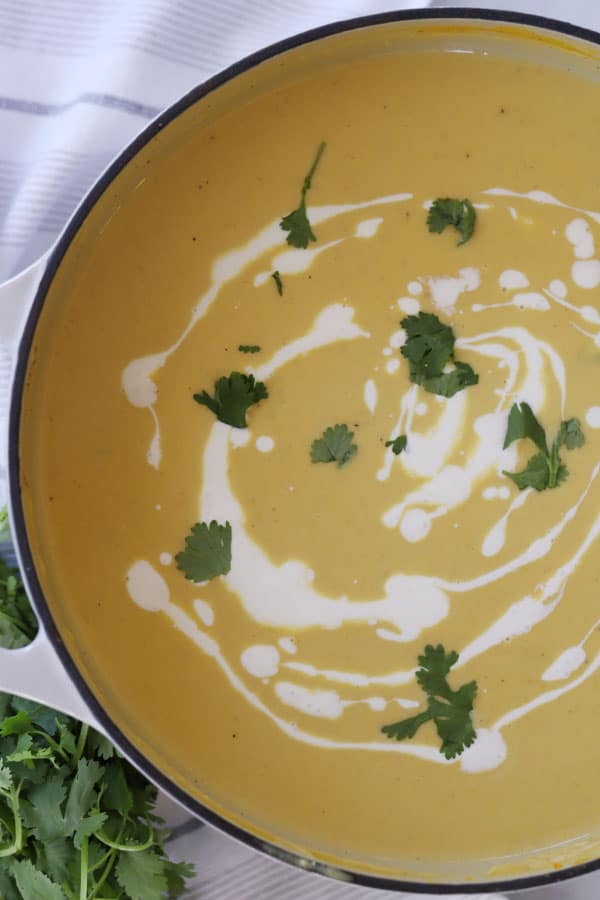 Roasted curry acorn squash soup in a dutch oven garnished with sour cream and fresh herbs.