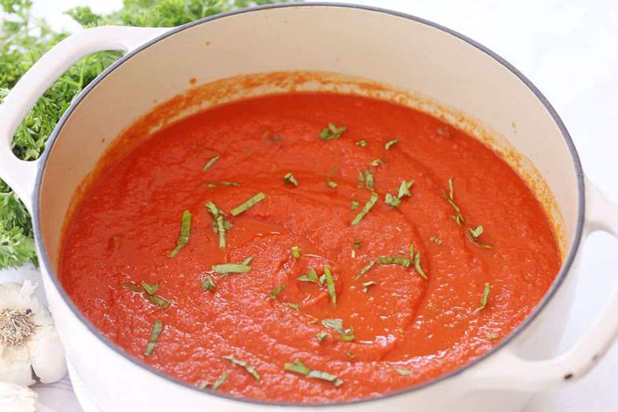 Homemade marinara sauce in a pot topped with fresh basil.