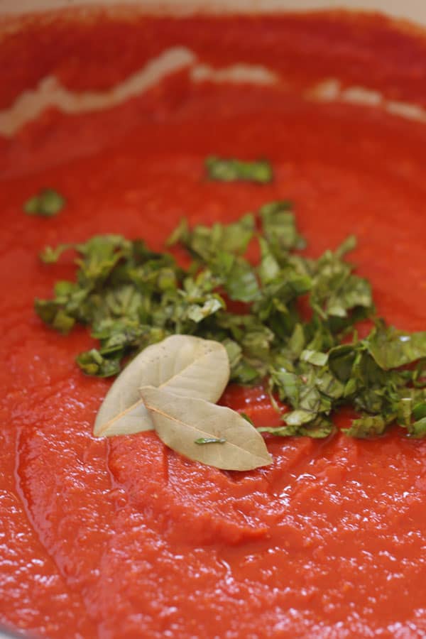 Marinara sauce in a pot topped with fresh basil and bay leaves.