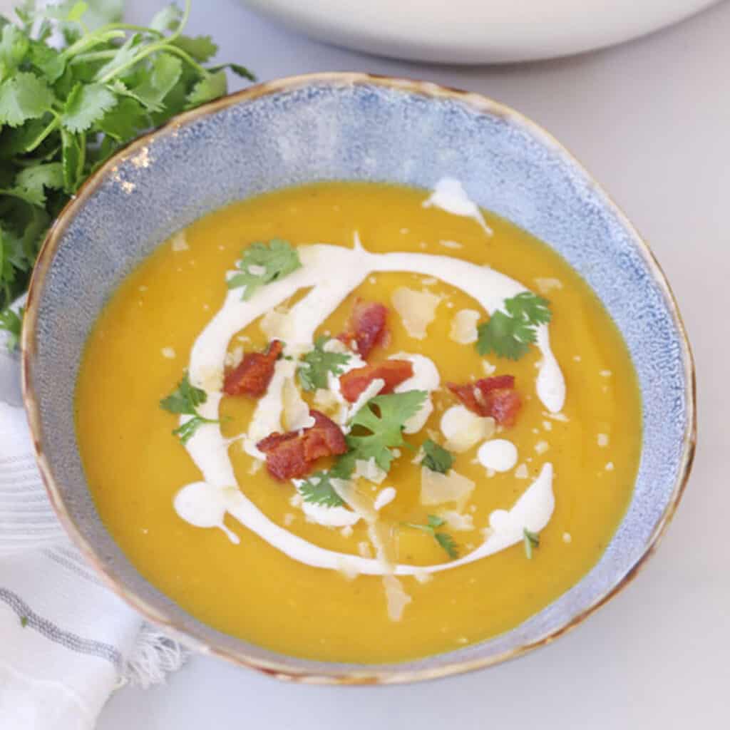 A serving bowl full of soup garnished with bacon, cilantro and creamy sauce.