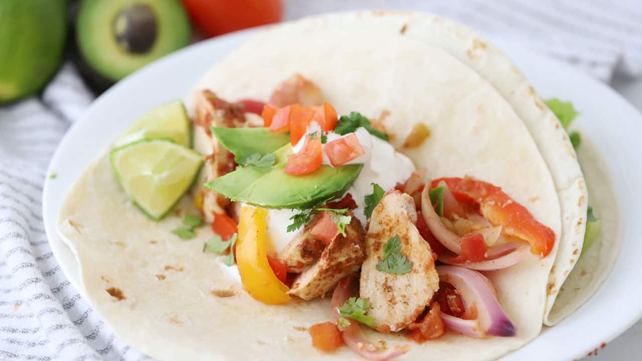 Chicken fajitas in a flour tortilla with toppings on a white plate.
