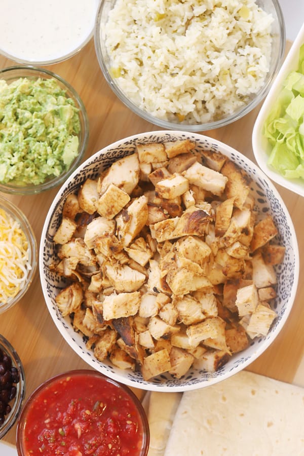 Chipotle chicken in a bowl with side bowls of cheese, guacamole and more.