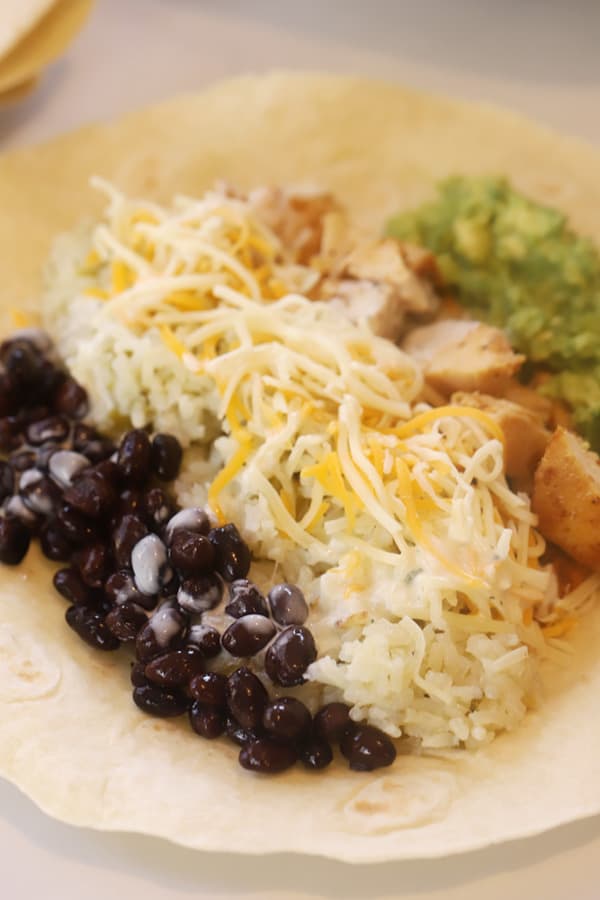 A flour tortilla filled with black beans, rice, shredded cheese, chicken and guacamole, about to be rolled into a chipote chicken burrito recipe.