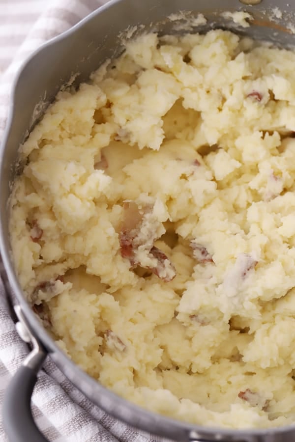 mashed red potatoes, mashed with a potato masher, in a silver pot