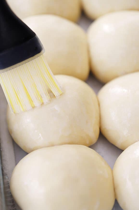 Quick and easy dinner rolls being brushed with butter before baking, the best recipe for quick dinner rolls.